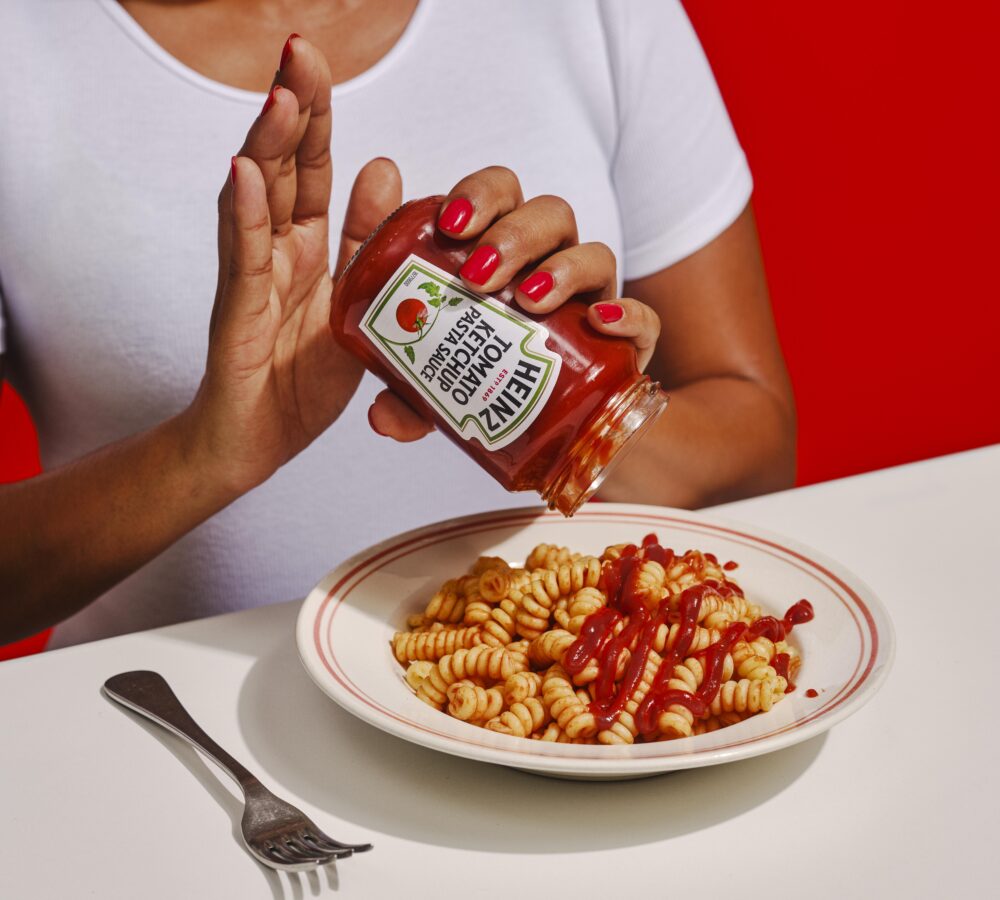 Woman in white top tipping Heinz Tomato Ketchup Pasta Sauce onto plate of pasta