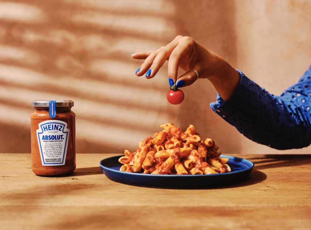 Woman holding tomato over pasta, with Heinz x Absolut Tomato Vodka Pasta Sauce next to it