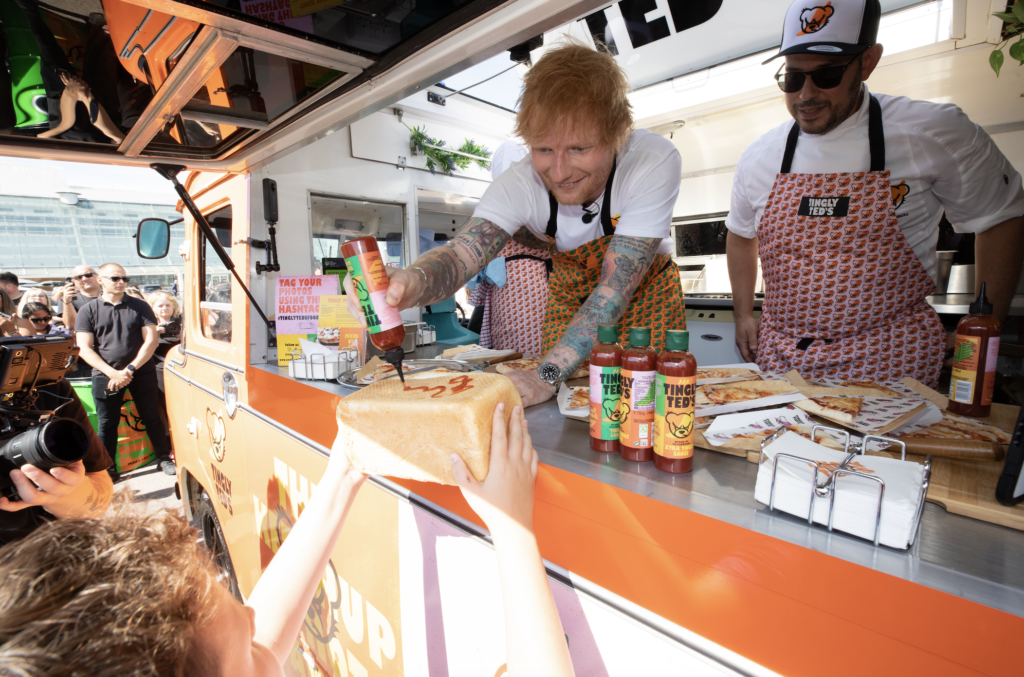 Ed Sheeran signing bread loaf with hot sauce in Tingly Ted's food truck